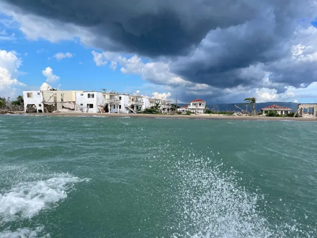 Coastal buildings beyond turquoise sea under dramatic clouds