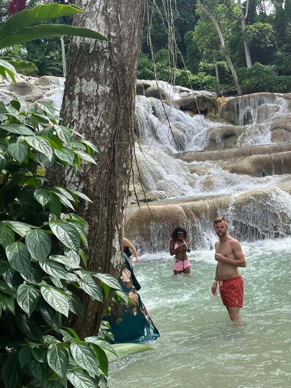 Visitors in waterfall pools framed by green leaves