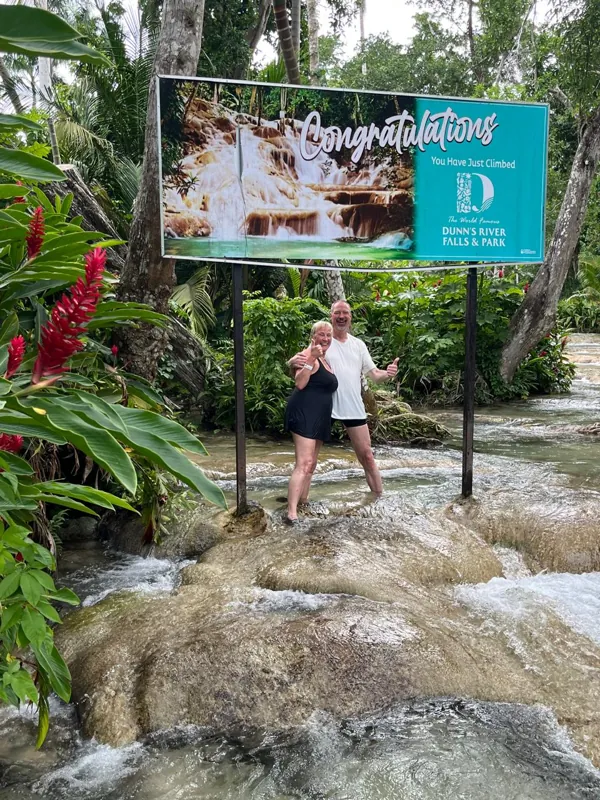 Two guests smiling below the Dunn’s River Falls sign